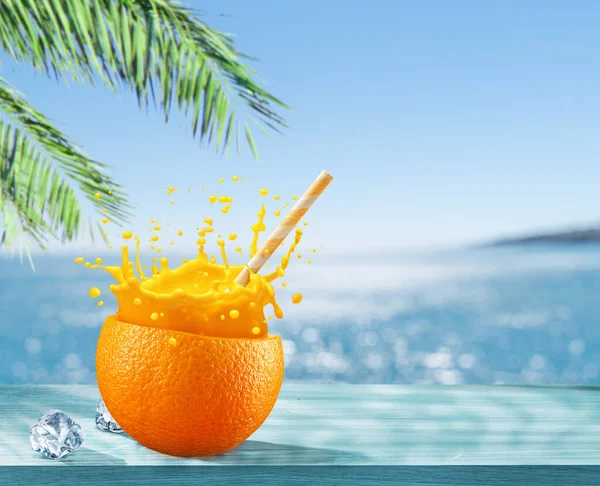 Orange fruit as the cup with orange juice splash and straw. Blue sparkling sea at the background. Drink concept.