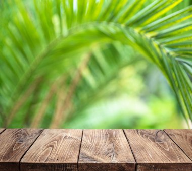 Empty old wooden plank table top and blurred green palm leaves at the background. Place for your product display. 