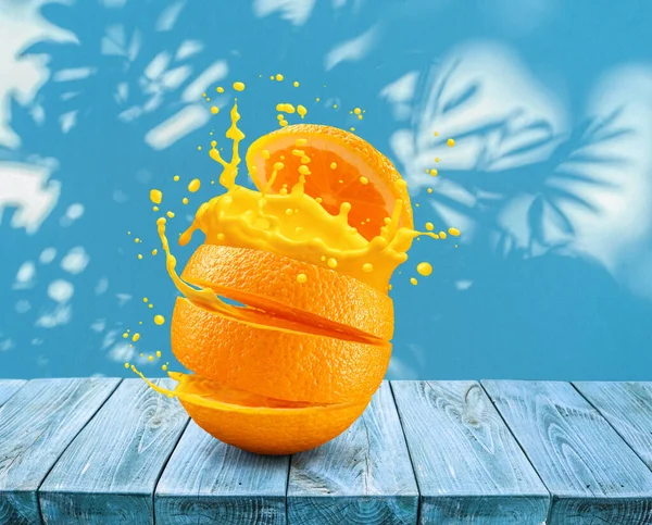 Sliced orange fruit splashing about orange juice on blue table and wall with leaf shadows at the background.