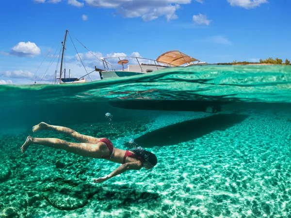 女性ダイバーは美しい海のビーチでシュノーケリングをしています 写真の下半分は海底で 上にはヨットと美しい空のある海岸があります — ストック写真