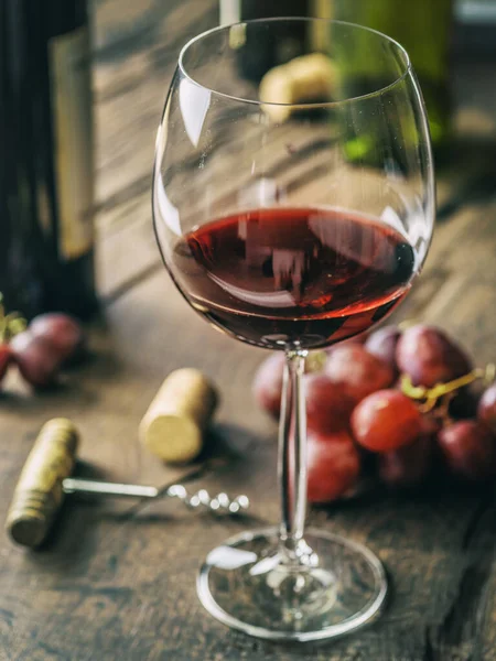 Wine testing. Wine glass, grapes and bottle opener on old wooden table.