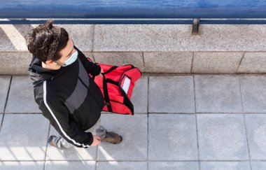 Kırmızı çantalı teslimatçı yüz maskesiyle eve teslimat yapmaya gidiyor.