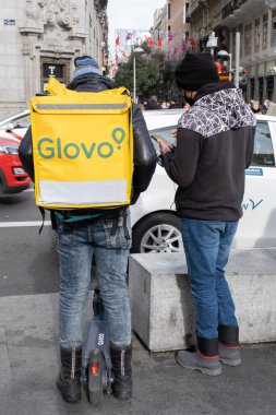Madrid, İspanya - 8 Ocak 2022: Sarı sırt çantalı kurye ve scooter Madrid sokaklarında