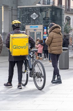Madrid, İspanya - 8 Ocak 2022: Sarı sırt çantalı kurye ve scooter Madrid sokaklarında