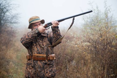 Avcı kıyafetli gri sakallı avcı çift namlulu tüfekle nişan alma kablosu yapıyor. 