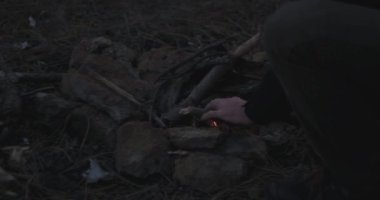 Karanlık bir zamanda bir adam kamp ateşini yakıyor.