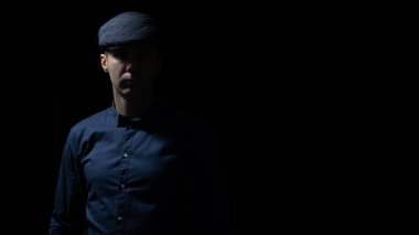 Kepi ve mavi gömlekli adam karanlıkta, aydınlıkta ve gölgelerde kalıyor. 