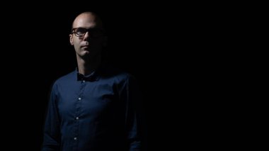 Gözlüklü ve mavi gömlekli adam karanlıkta, aydınlıkta ve gölgelerde kalıyor. 