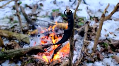 Karambit bıçağı, karanlık karlı ormanda şenlik ateşinin önünde dalda.