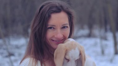 Kadın, karlı kış ormanında ceketli köpek yavrusuyla sarılıyor.