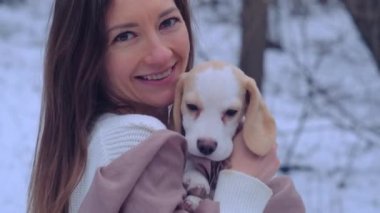 Kadın, karlı kış ormanında ceketli köpek yavrusuyla sarılıyor.