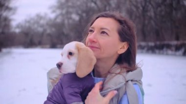 Kadın ceketli, buz tutmuş bir nehrin kıyısında sevimli bir köpek yavrusuyla sarılıyor.