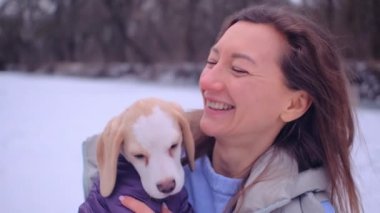 Kadın ceketli, buz tutmuş bir nehrin kıyısında sevimli bir köpek yavrusuyla sarılıyor.