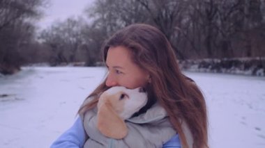 Kadın ceketli, buz tutmuş bir nehrin kıyısında sevimli bir köpek yavrusuyla sarılıyor.