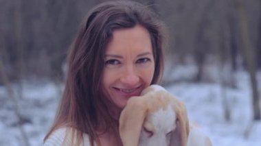 Kadın, karlı kış ormanında ceketli köpek yavrusuyla sarılıyor.