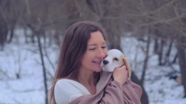 Kadın, karlı kış ormanında ceketli köpek yavrusuyla sarılıyor.