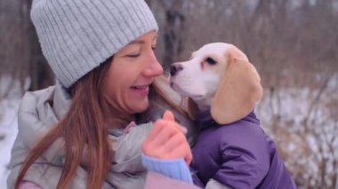 Kadın, karlı kış ormanında ceketli köpek yavrusuyla sarılıyor.