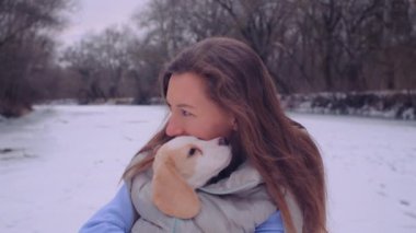 Kadın ceketli, buz tutmuş bir nehrin kıyısında sevimli bir köpek yavrusuyla sarılıyor.