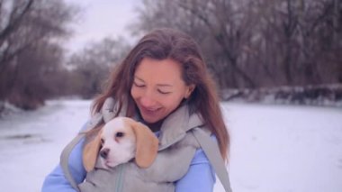 Kadın ceketli, buz tutmuş bir nehrin kıyısında sevimli bir köpek yavrusuyla sarılıyor.