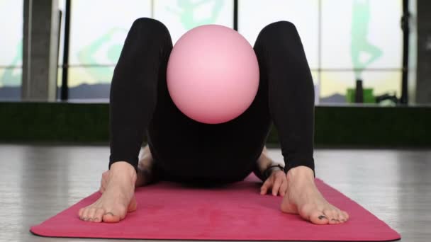 Frau mittleren Alters macht Pilates-Übungen mit einem Fitnessball auf der Matte im Studio