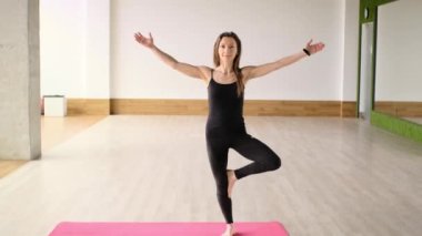 Orta yaşlı bir kadın stüdyodaki paspasın üzerinde barışçıl bir savaşçı Asana taklidi yapıyor.