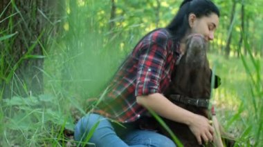 Kırmızı ekose gömlekli beyaz bir kadın yeşil parkta yaşlı bir labrador köpeğiyle oynuyor.