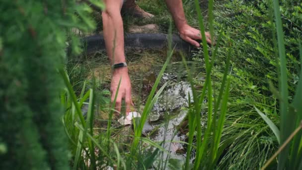 一个无法辨认的人正在用双手清扫花园的池塘 池塘是用蒂娜和泥土做的 手上拿着一个健身的手镯 — 图库视频影像