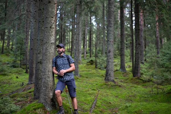 緑の山の森の中でハイカーのひげ男 キャップ ショートパンツ バックパックとトレッキングスティック付きのプレイシャツでドレスアップ — ストック写真