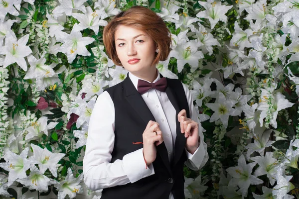 Mujer joven hermosa y de moda cerca de la pared de flores — Foto de Stock