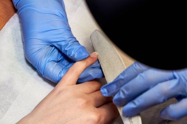 Bir manikür ustası tırnak törpüsüyle bir parmağı inceler güzellik ve sağlık alanında özel bir iş geliştirmek için.