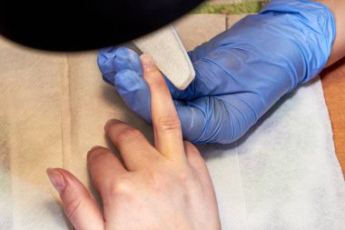 Manikür ustası tırnak törpüsüyle parmağı inceliyor.