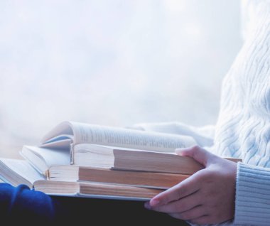 Beyaz yün kazaklı kadın elinde kitap tutarken yakından görülüyor. Kitap konsepti arka planının maketi için boş alan.