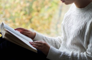 Beyaz yün kazaklı kadın elinde kitap tutarken yakından görülüyor. Kitap konsepti arka planının maketi için boş alan.