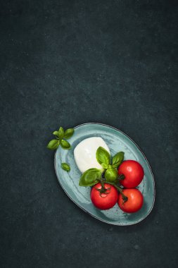 Taze vişneli domates, fesleğen, siyah taş masada mozzarella peyniri. Sağlıklı İtalyan geleneksel salata malzemeleri. Organik Akdeniz mutfağı konsepti, daire, yakın plan. Yaz Yemeği.