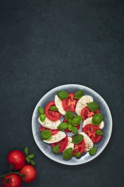 Taze vişneli domates, fesleğen, siyah taş masada mozzarella peyniri. Sağlıklı İtalyan geleneksel salata malzemeleri. Organik Akdeniz mutfağı konsepti, daire, yakın plan. Yaz Yemeği.