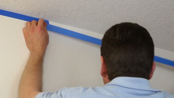 Homme appliquant la bande du peintre bleu sur le mur sous le plafond — Video