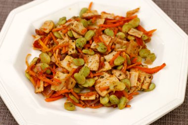 Bir tabakta servis edilen organik hindi, havuç, fasulye, domates, soğan ve maydanozdan oluşan pişirilmiş yemek. Kahverengi bir paspasın üzerinde beyaz bir tabakta birkaç sebzeli organik hindi.