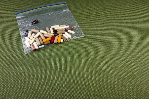 An assortment of health supplements in a clear sandwich plastic bag on a green tablecloth. Over three dozen health supplements in capsules, tablets and pills in a clear plastic bag when traveling.