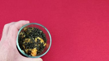 Papaya tohumları küçük bir cam kasede sol elle toplanıyor ve farklı açılardan izleyicilere gösteriliyor. Papaya tohumları ve beyaz bir erkek tarafından gösterilen küçük bir cam kasede biraz papaya meyvesi özü..