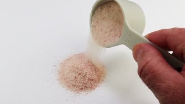 Yetişkin erkek, beyaz beyaz beyaz kağıda ince buğday pembesi Himalaya tuz kristalleri döküyor. Himalaya pembe tuzu, çeyrek fincandan beyaz kağıda yavaşça dökülüyor.