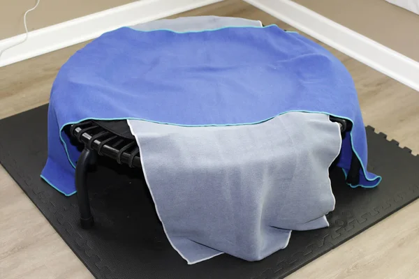一个蓝色和一个灰色的运动毛巾垫覆盖一个圆形黑色蹦极绳跳板的运动设备 在覆盖在运动毛巾上的黑色垫子上的圆形黑色篮板运动器械 可进行特写 — 图库照片