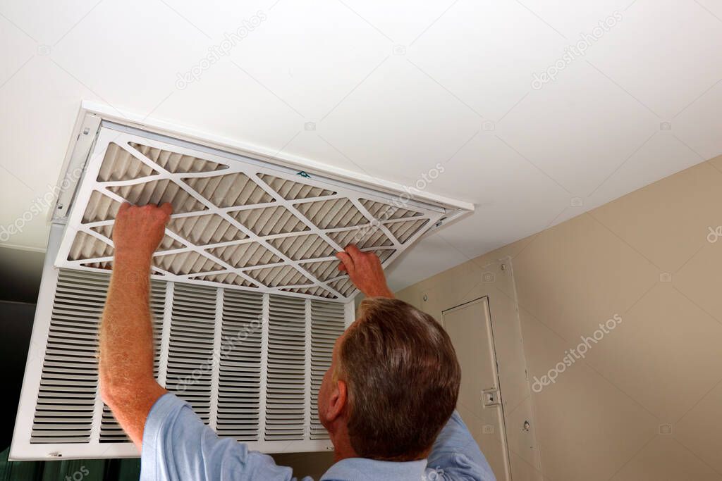 Dirty air filter being removed from a home furnace air intake vent by an adult white male close-up. Adult white male removing a dirty air filter from a furnace air duct intake vent in a home ceiling.