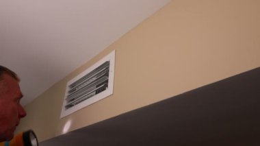 Flashlight 'lı bir adam bakım için havalandırma kanalını inceliyor. Erkek, kalitesini ölçmek için el feneriyle küçük bir havalandırma deliğine bakıyor. Ev sahibi küçük bir havalandırma deliğinin içini inceliyor ve her türlü bakım için bir el feneri var..