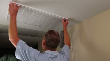 Adult Male Cleaning Dusting Air Duct Vent Grid Inside and Exterior.Mature male dusting inside and outside of his air intake grid in a home furnace ceiling. Entryway ceiling air intake vent to furnace large grid being dusted inside and out in a home