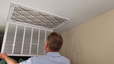 Replacing Dirty Air Filter with a Clean Air Filter. Air filter being replaced from a clean to dirty one in monthly maintenance as a home furnace by a home owner. Maintenance replacement of an air filter in a ceiling of a condo by a mature adult male.