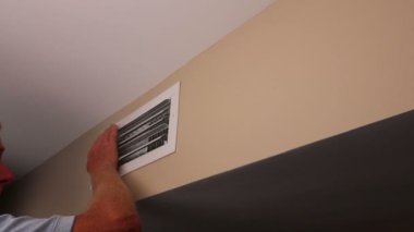 Yetişkin erkek, bir ve iki elini küçük bir dikdörtgen havalandırma kanalına yerleştirir. Duvarın tepesinde, hava akışını hisseder. Olgun bir erkek, elleri havalandırma borusunun önünde. Havanın akışını hissediyor.