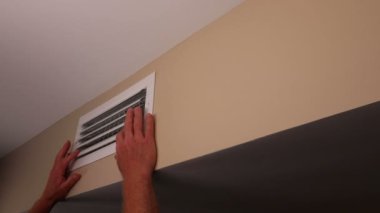 Beyaz İnsan Elleri Havalandırmayı Kapıyor Ayarlanabilir Kayıt Bıçağı. İki el dikdörtgen bir havalandırmayı kapatıyor, ayarlanabilir kayıt bıçakları evdeki duvarda, tek tek tavana yakın. Olgun erkek elleri havalandırma borularını birer birer kapatıyor.