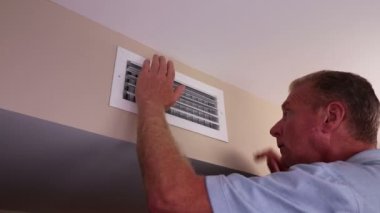 From the left side a homeowner moves both hands in front of a air duct vent to feel for air circulation. Man feeling for air circulation from an air duct outflow vent on a wall near a ceiling