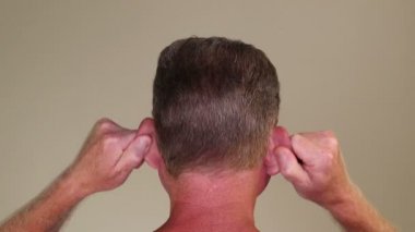 Yetişkin bir beyaz adamın iki kulağına da aynı anda masaj yapması. 50-59 yaşlarında beyaz bir erkek, elleri kapalı olarak iki kulağına da masaj yapıyor.