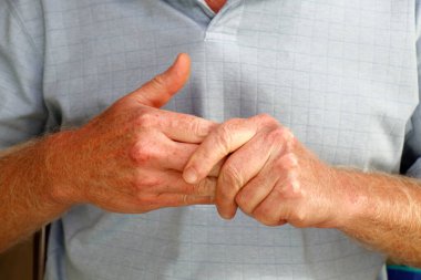 Close-up of mature caucasian males left hand massaging the fingers of his right hand to ease any pain and soreness in muscles and joints. Left hand of a man massaging his right hand fingers close-up.